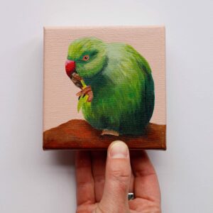 Klein schilderij van een halsbandparkiet die eten vasthoudt met één poot tegen een zachte poederroze achtergrond