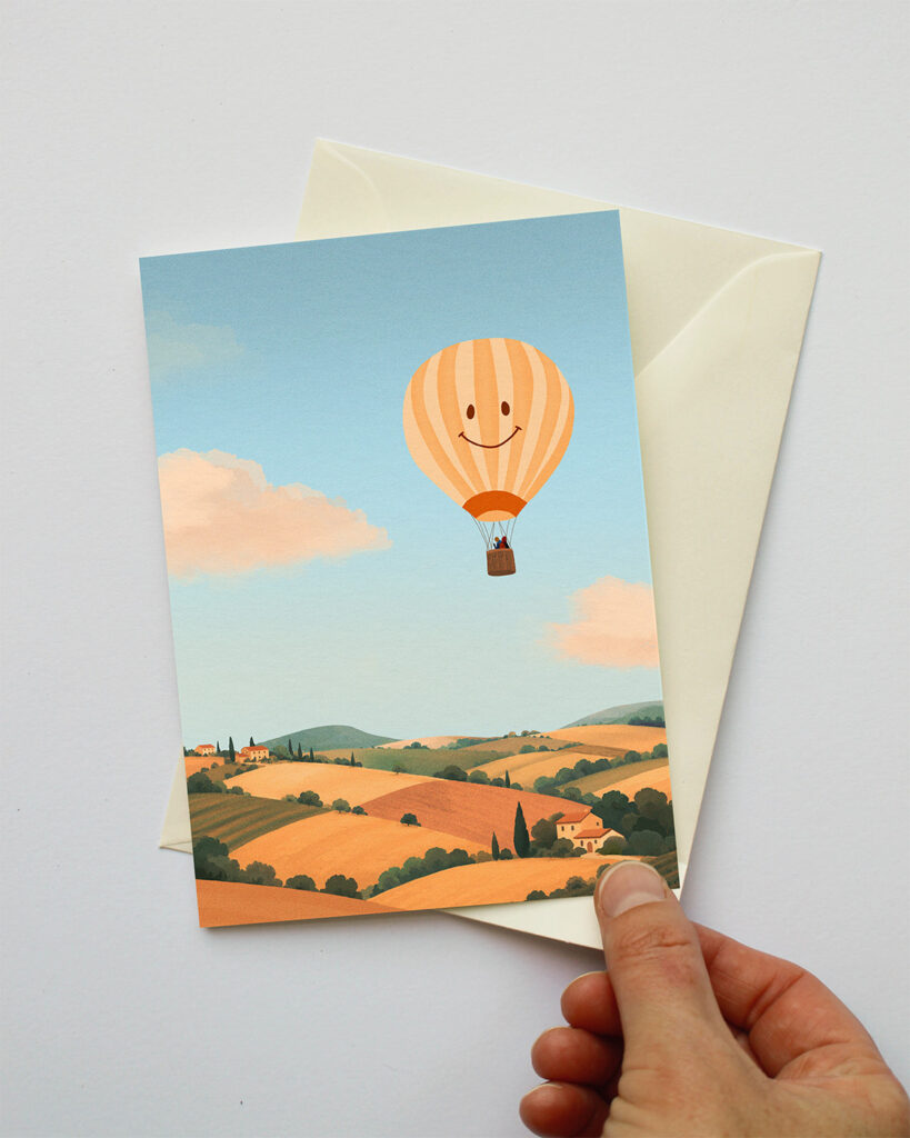Wenskaart met een glimlachende luchtballon boven een landschap.