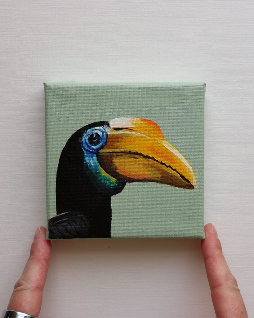Klein schilderij van een neushoornvogel met geel-oranje snavel tegen een zachte saliegroene achtergrond