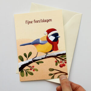 Kerstkaart met koolmees met rode kerstmuts en sjaal op een besneeuwde tak en de tekst "Fijne feestdagen"